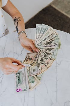 Close-up of hands holding and counting various US dollar bills on a marble table.
