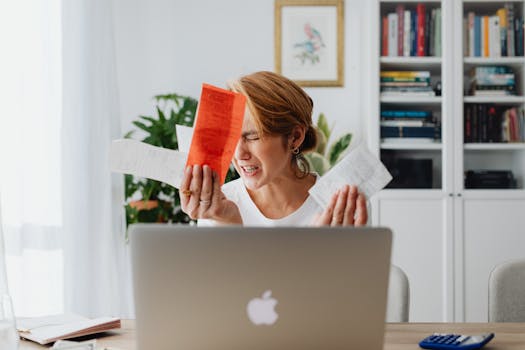 Frustrated woman managing finances, surrounded by bills and a laptop, looking distressed.